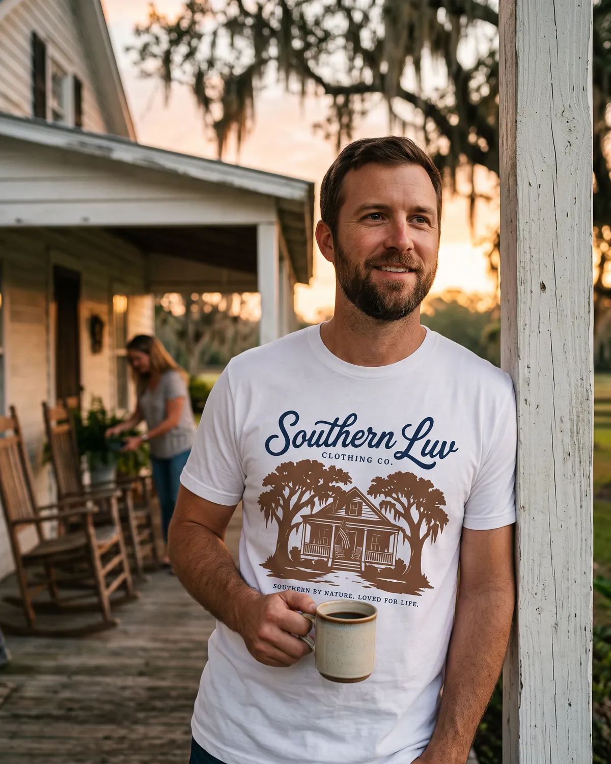 Man in a Southern Luv tee leaning on a farmhouse porch post at sunrise