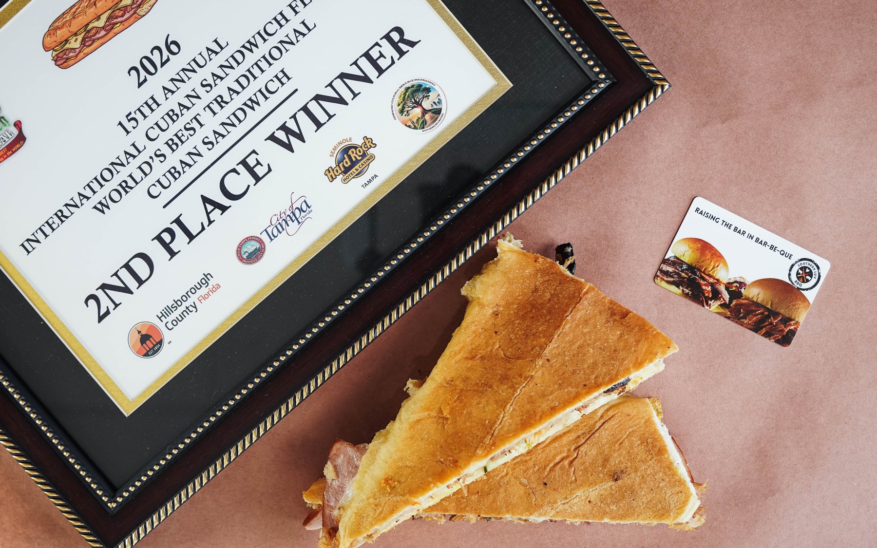 The 2026 World’s Best Traditional Cuban Sandwich second-place award beside Southern Luv’s pressed Cuban