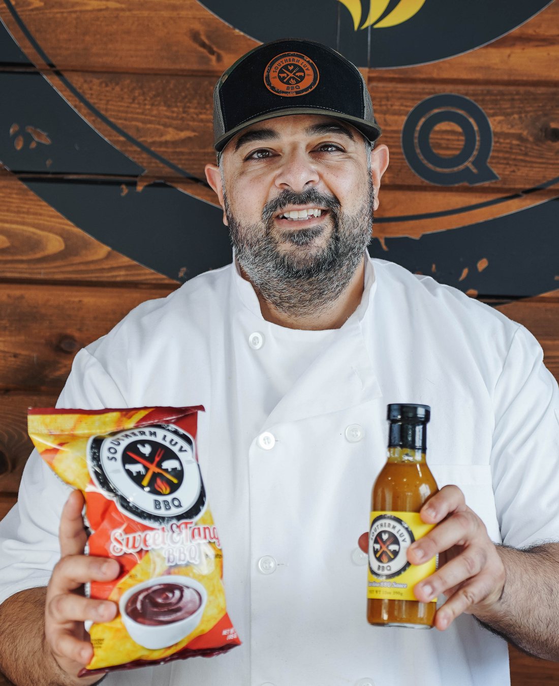 Chef Essi Tadrus in chef whites holding Southern Luv BBQ sauce and chips